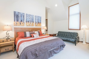 Une chambre à coucher avec un grand lit, deux tables de chevet, une chaise et des œuvres d’art accrochées au mur.