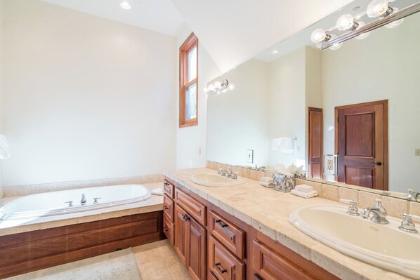 Un baño con una bañera grande, dos lavamanos, muebles de madera y un espejo con luces.