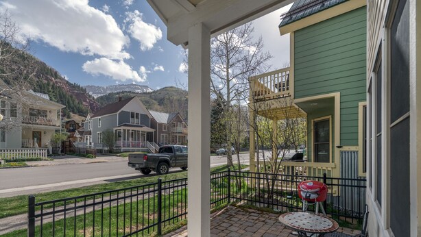 A porch with a table and chairs, a red grill, and a view of a street with houses and mountains. - Downtown Telluride Townhome | Walk to Gondola | 3BR, Steam Shower, Parking (Telluride)