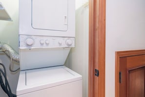 A white front-loading washing machine with control knobs, a dryer, and a wooden door in a laundry room.