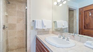 Ein Badezimmer mit Dusche, Waschbecken, einem beleuchteten Spiegel und einem Holzkorpus.