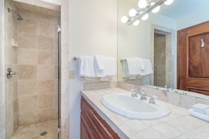 Une salle de bain avec une douche, un lavabo, un miroir avec éclairage et un meuble en bois.