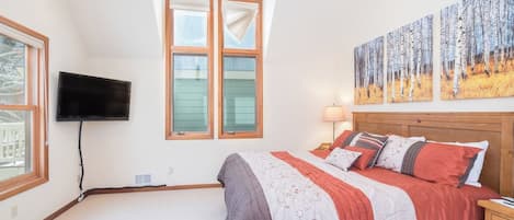 A bedroom with a bed, a television mounted on the wall, and a window with curtains.