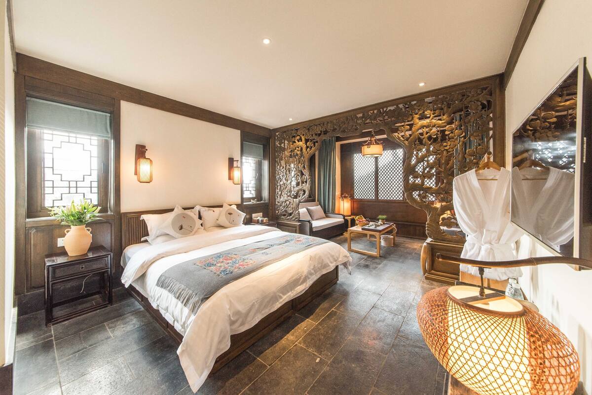 A modern bedroom with a large bed, a sitting area, and a decorative wall.
