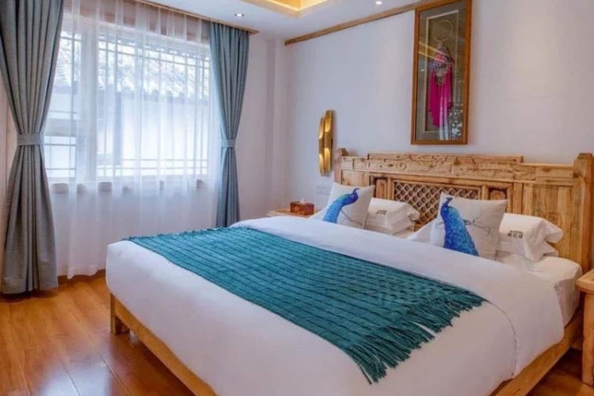A bedroom with a wooden ceiling, a large bed with white bedding and blue pillows, a nightstand, and a window with curtains.