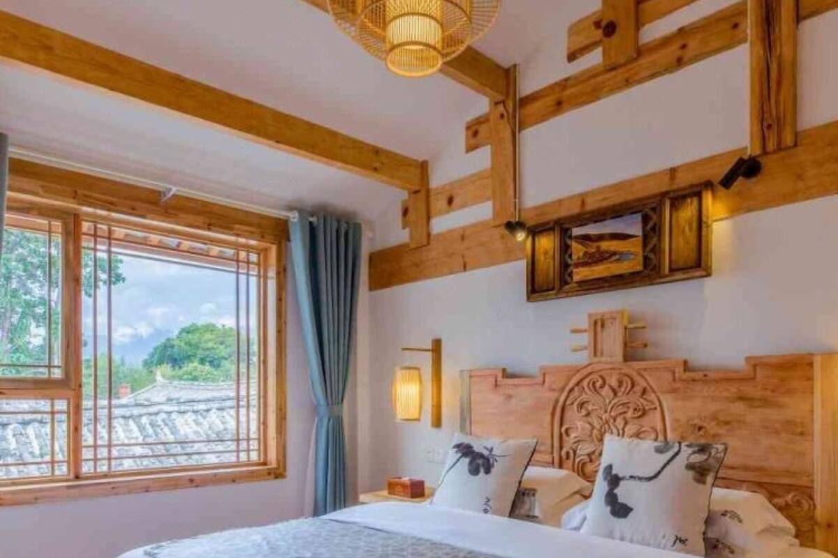 A bedroom with a large bed, wooden beams, a window with a view, and a decorative headboard.
