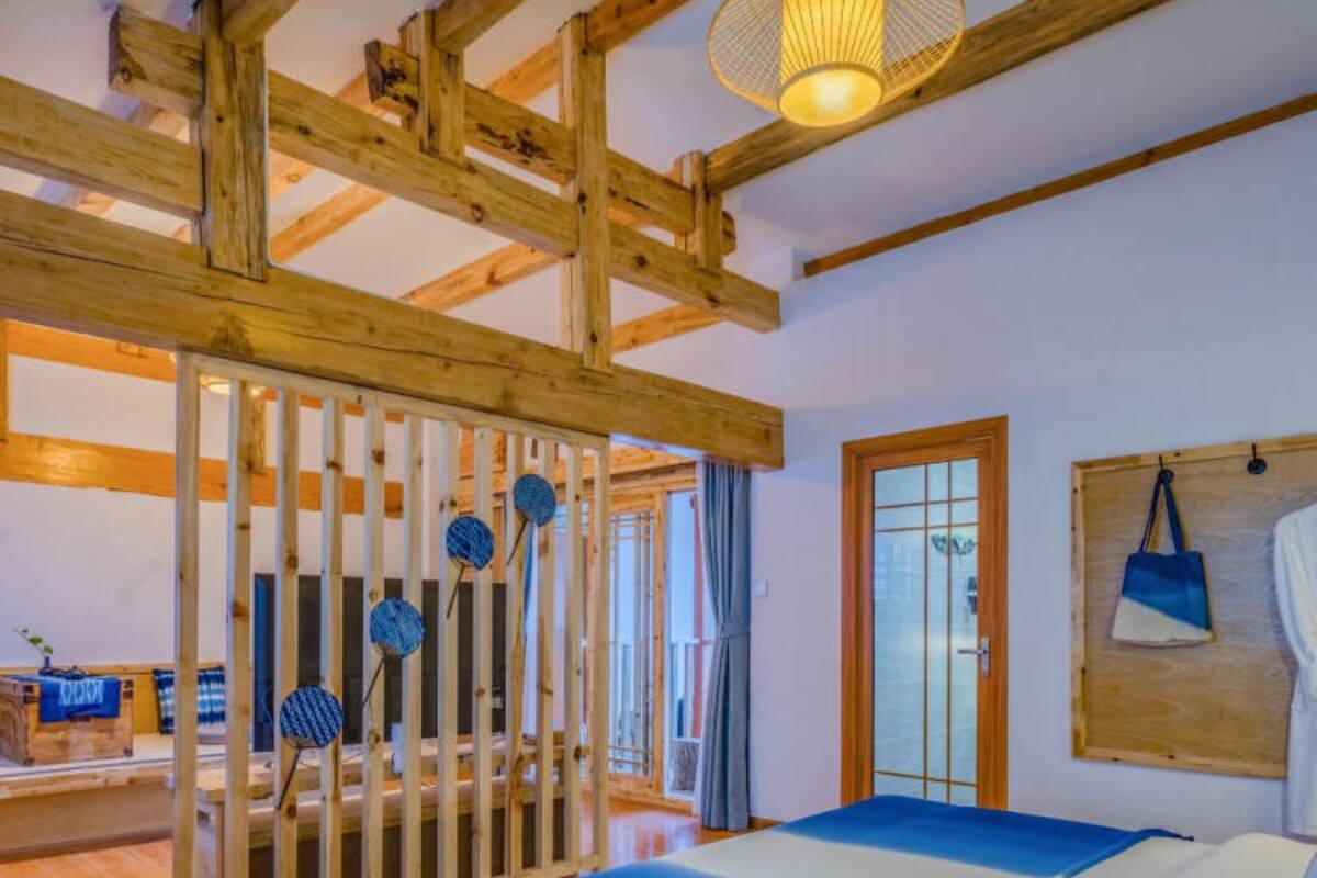 A room with a wooden ceiling, a bed with blue bedding, a wooden wardrobe, and a hanging bag.
