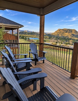 Eine überdachte Terrasse mit Adirondack-Stühlen und Blick auf einen See und Berge.