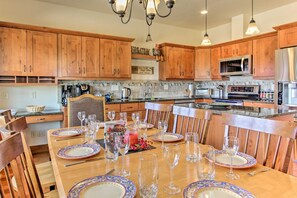 A kitchen with wooden cabinets, a dining table set with plates and glasses, and various kitchen appliances. - Rocky Mountain Hideaway | Scenic Views & Cozy Retreat (Estes Park)