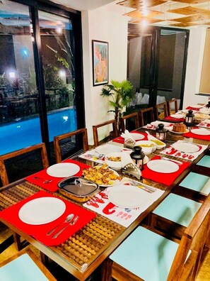 A dining area with a long table set for multiple guests, featuring a view of a pool outside. - Half Hotel (Candolim)