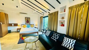 A modern hotel room with a bed, a sofa, a small round table, and a bookshelf. - Half Hotel (Candolim)
