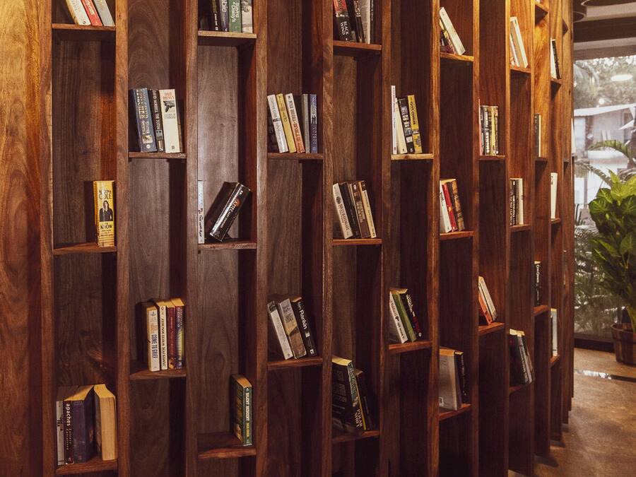 Estante de madeira com livros em um ambiente bem iluminado e com piso de azulejos.