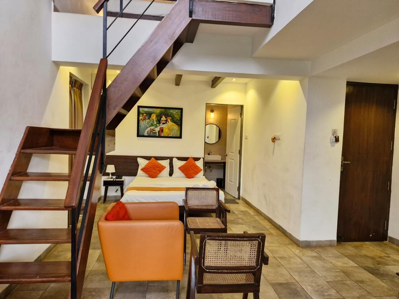 A bedroom with a wooden staircase, a bed with orange pillows, a sofa, and a chair.