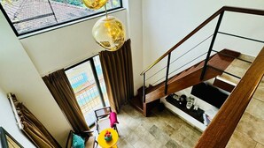 A spacious living area with a high ceiling, a staircase, and a view of palm trees outside. - Half Hotel (Candolim)
