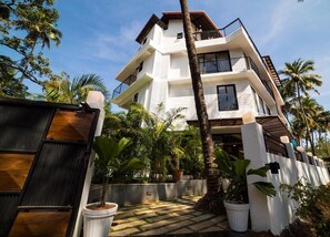 A multi-story white building with balconies, surrounded by palm trees and potted plants. - Half Hotel (Candolim)