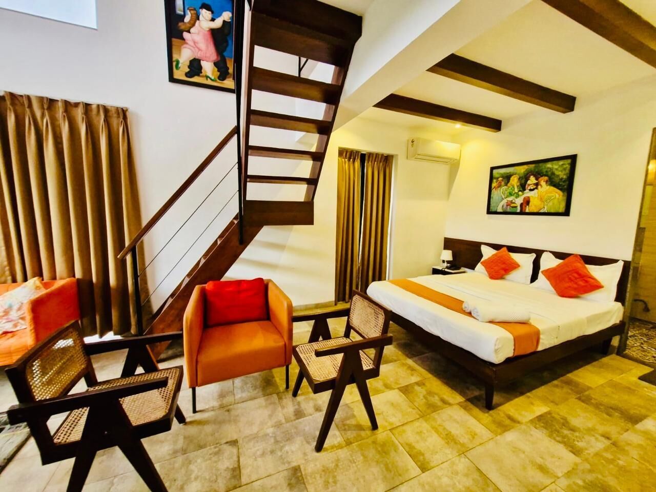 A hotel room with a bed, a sofa, a chair, a table, a staircase, and a painting on the wall.