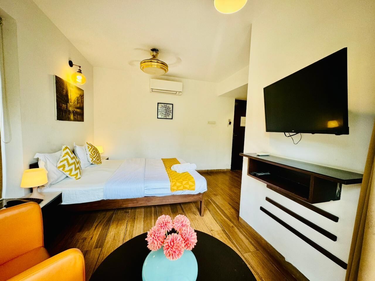 A hotel room with a bed, a TV mounted on the wall, a desk with a lamp, and a chair.
