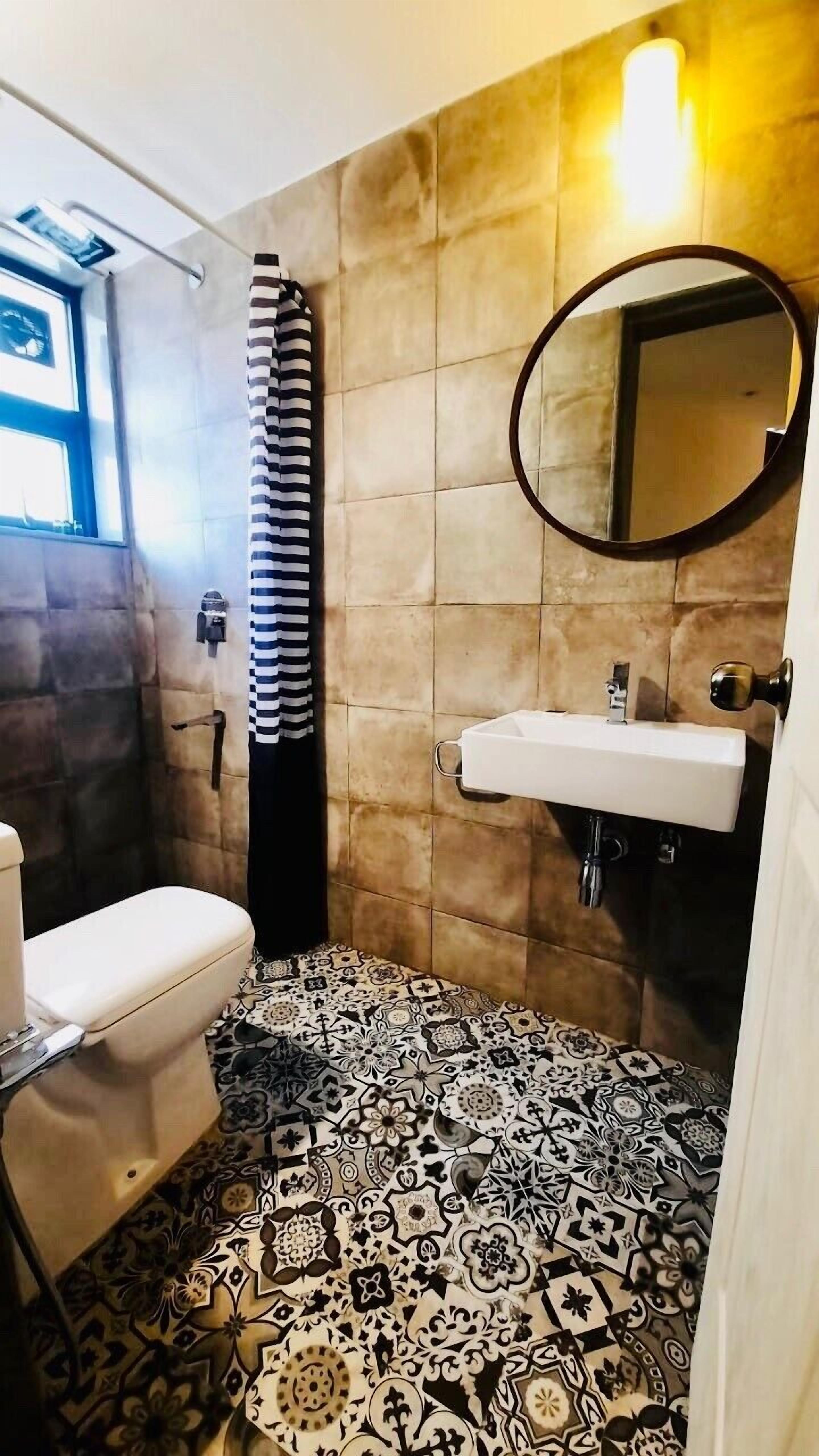 A bathroom with a toilet, a sink, a mirror, and patterned tiles on the floor.