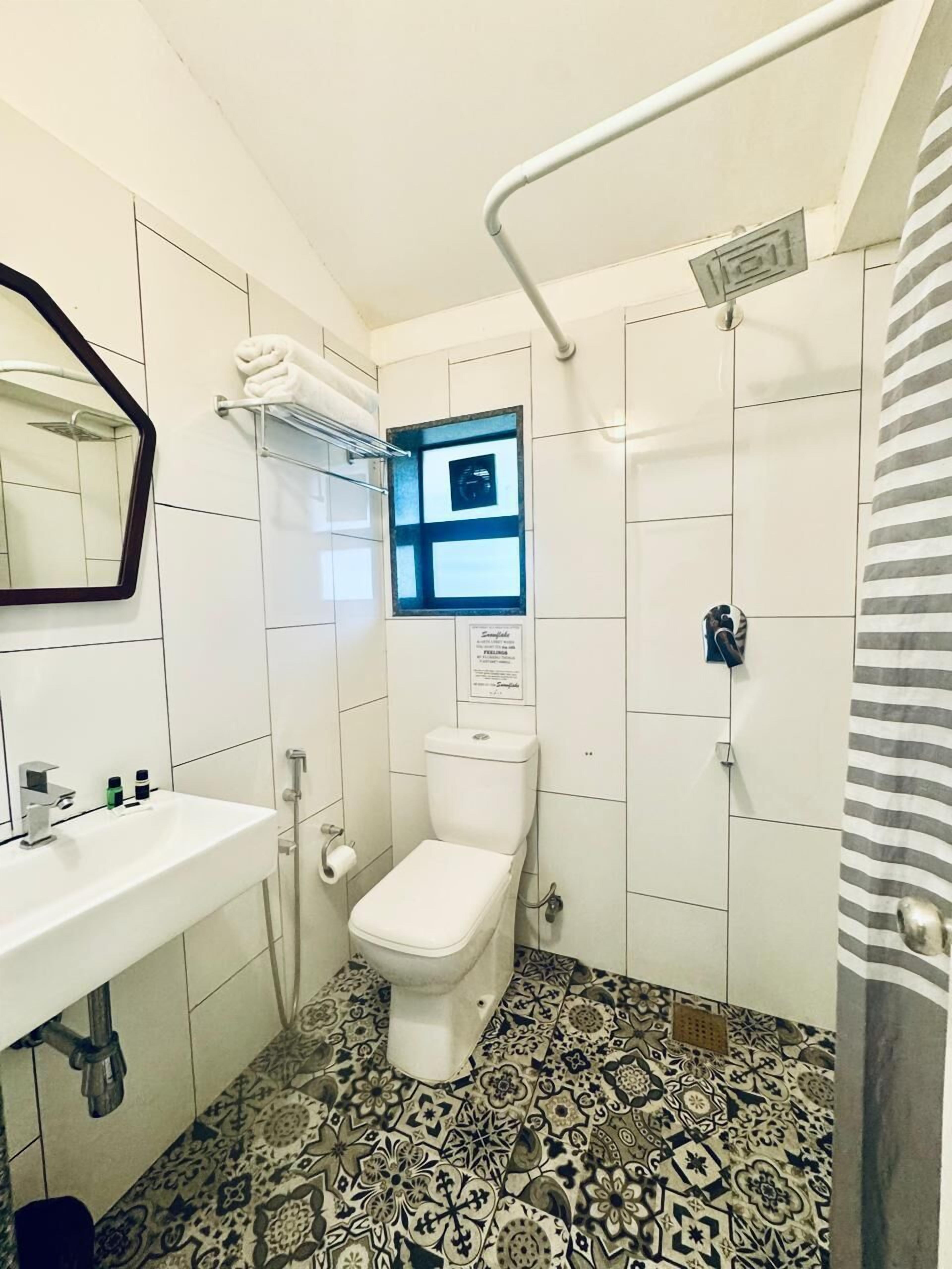 Un baño con inodoro blanco, lavamanos con espejo y baldosas de suelo estampadas.