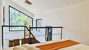 A modern bedroom with a large bed, a view of greenery through the windows, and a unique metal headboard structure. - Half Hotel (Candolim)