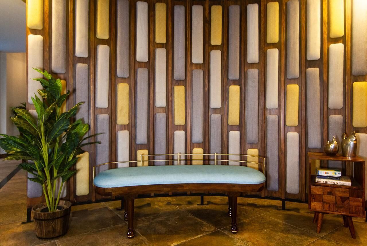 A room with a wooden bench, a potted plant, and a decorative wall with vertical panels.