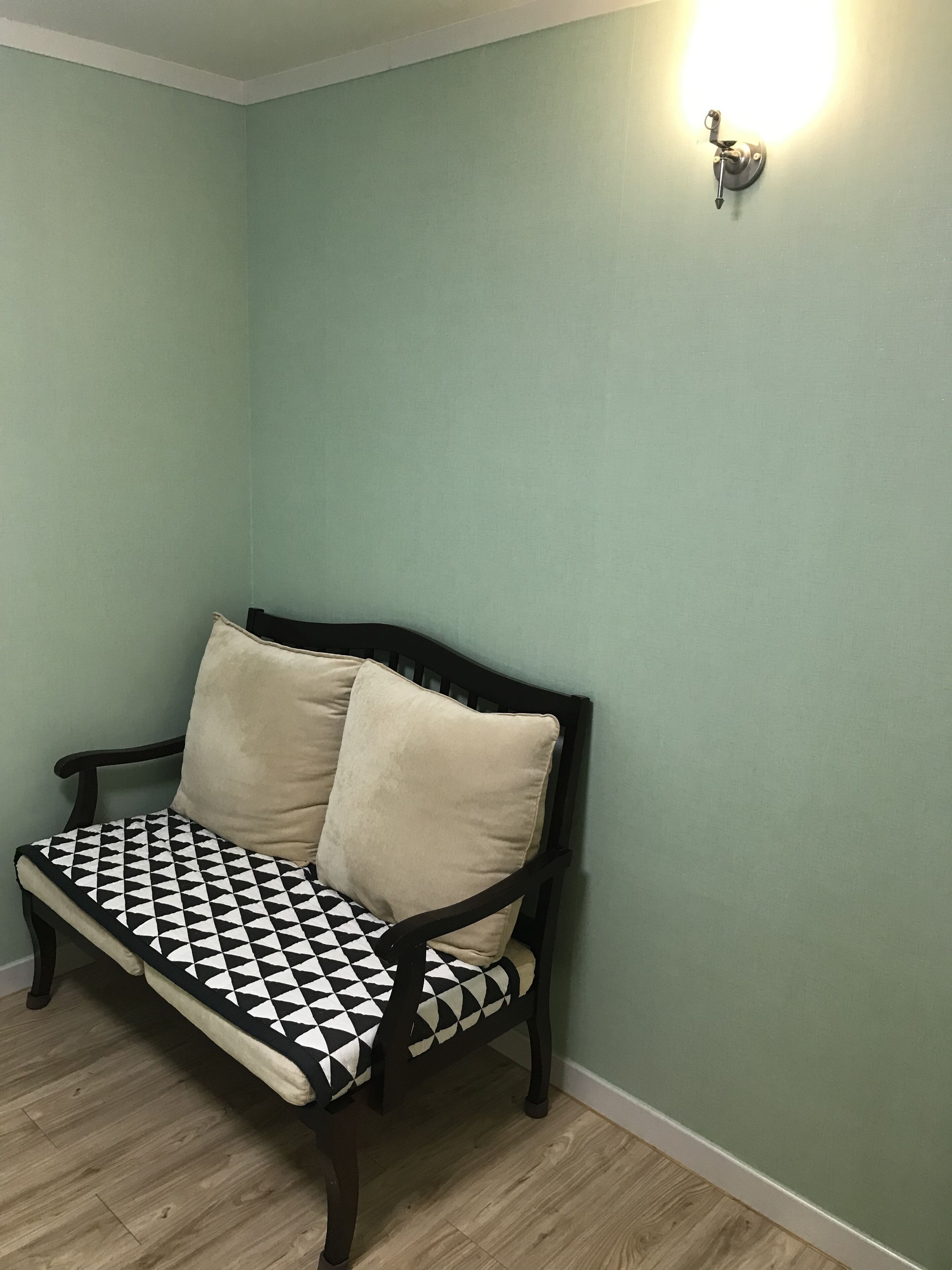 Quarto nos fundos com parede verde clara, piso de madeira e um banco preto e branco com dois apoios.