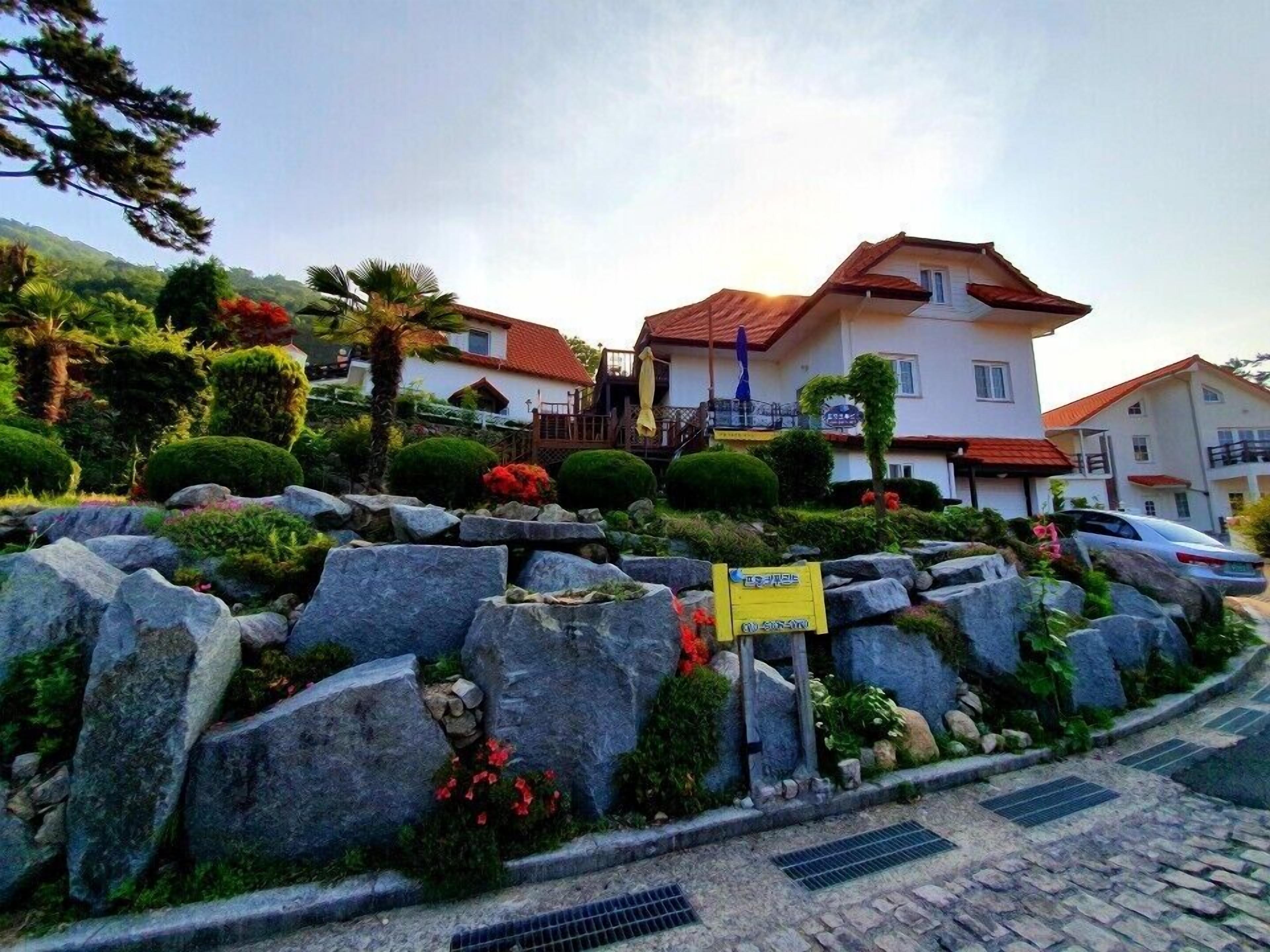 Un edificio residencial con techo de tejas rojas, rodeado de jardines ajardinados con rocas y arbustos.