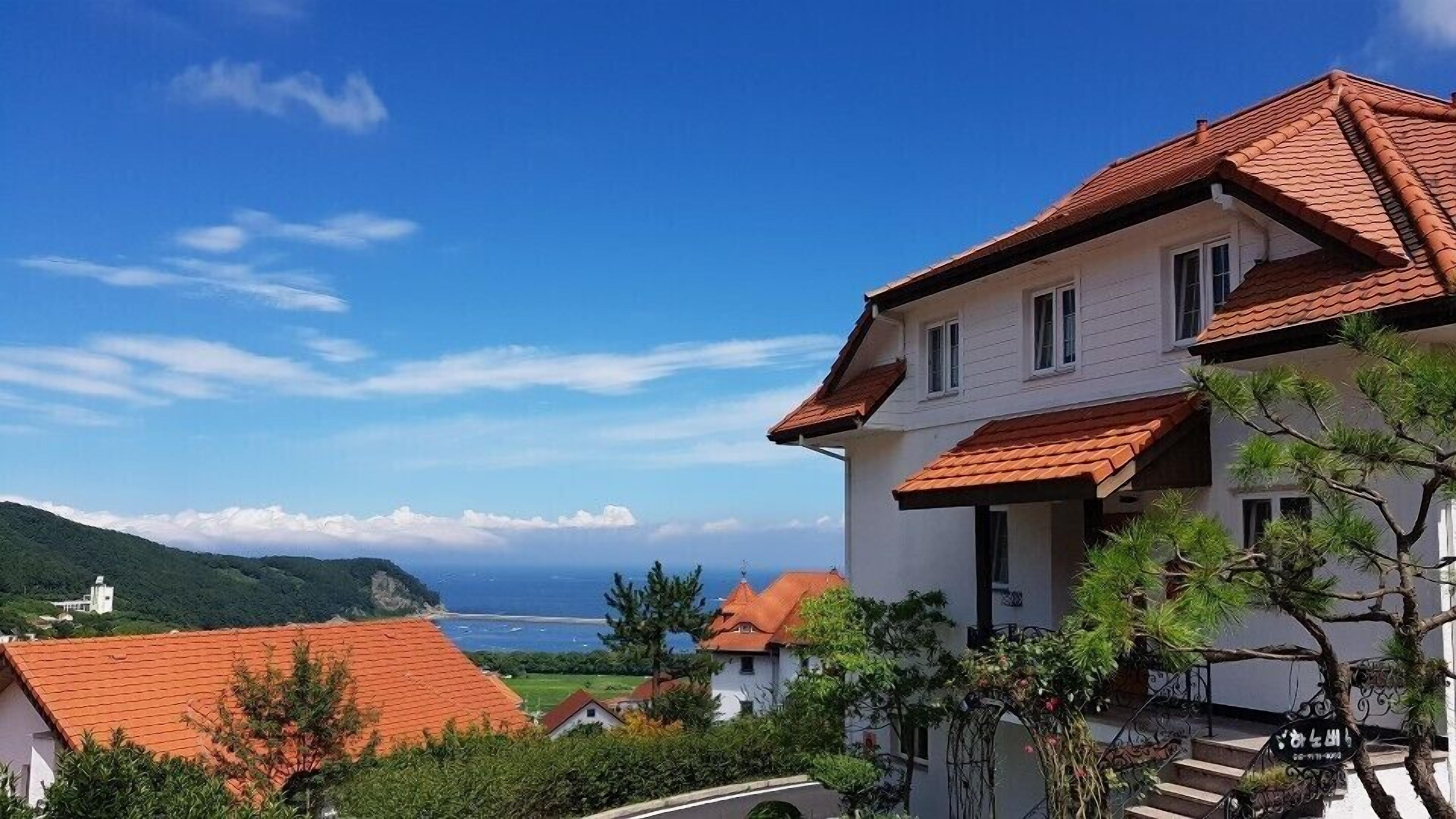 A coastal building with a red-tiled roof, white walls, and a balcony.