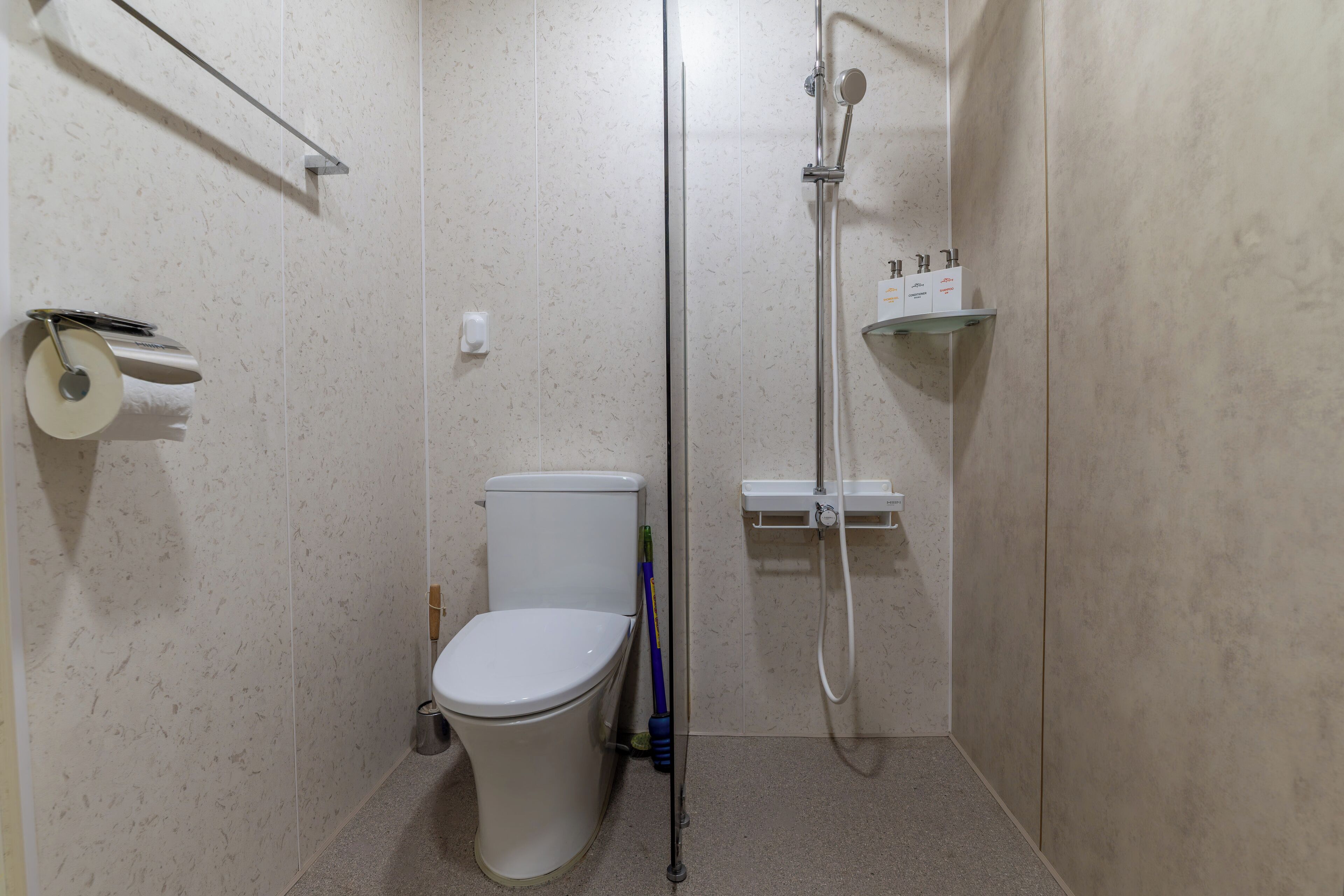 A small, modern bathroom with a toilet, a shower, and a shelf with toiletries.