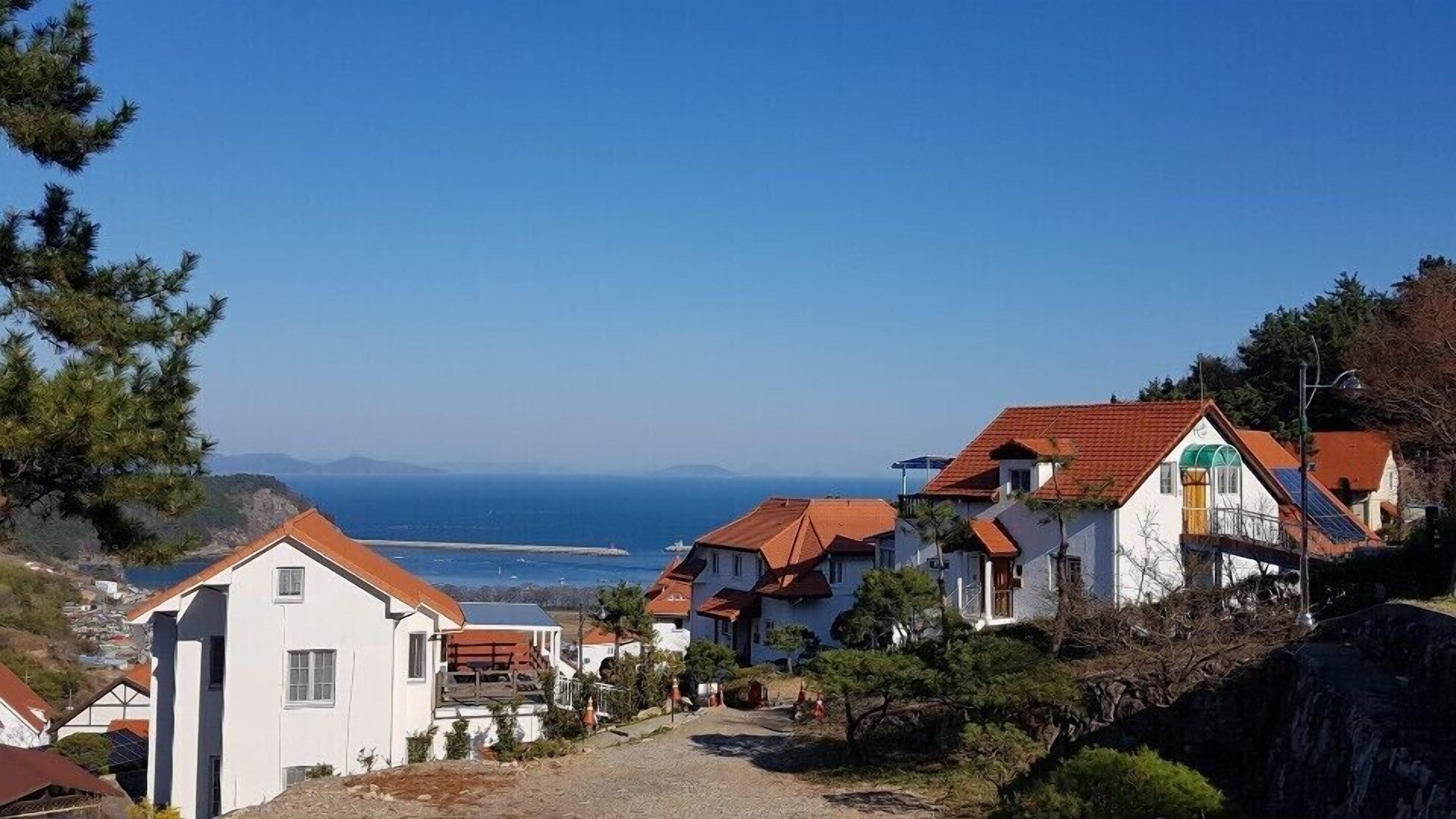 A coastal village with white buildings and red roofs, a clear blue sky, and a view of the sea.