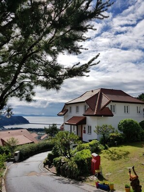 A white two-story house with a red roof, surrounded by greenery and a view of the sea. - Namhae German Village Frankfurt Story (Namhae)