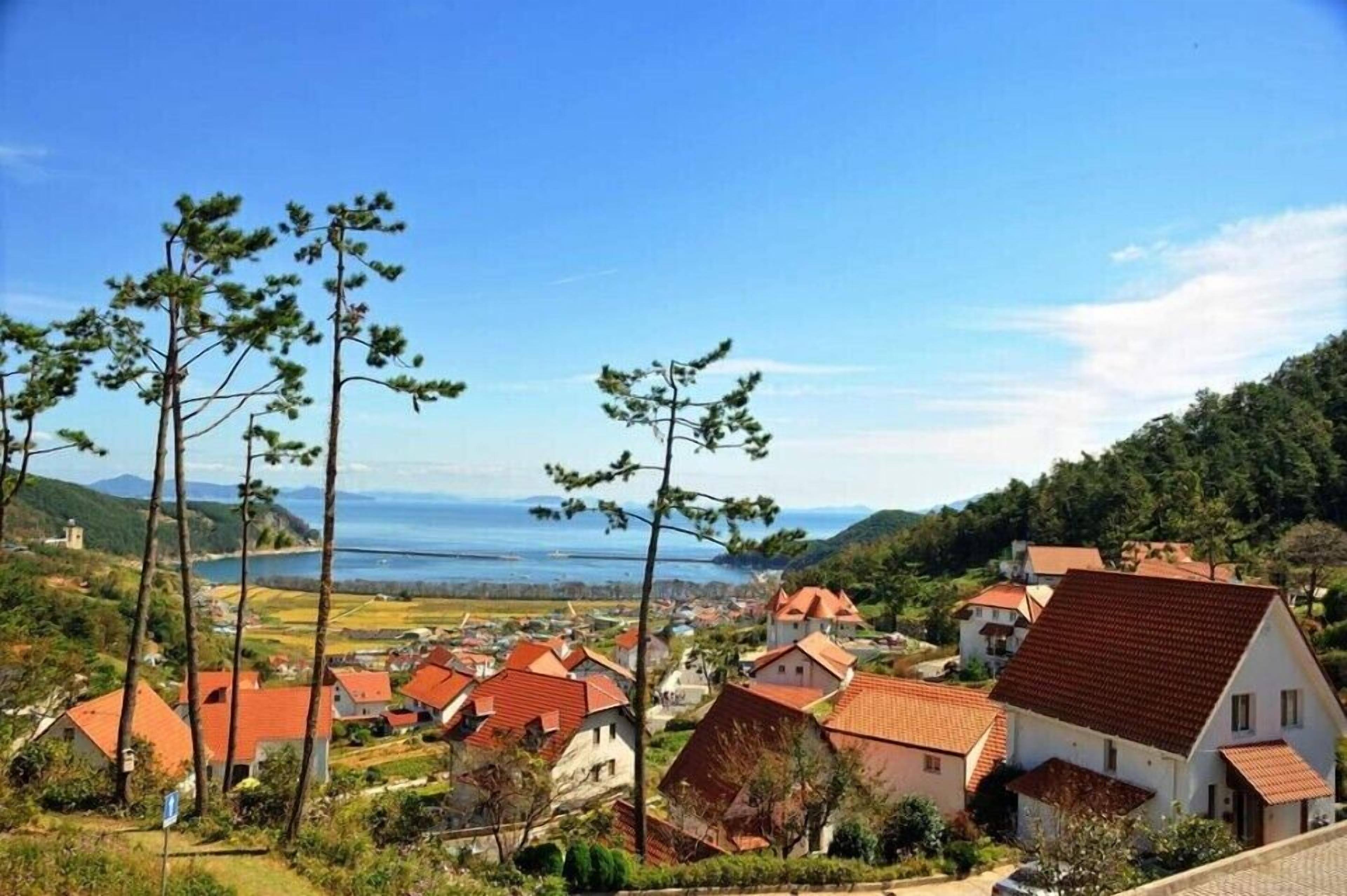 A coastal village with traditional red-roofed houses, a clear blue sky, and a view of the sea.