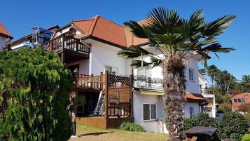 Ein zweistöckiges Gebäude mit Balkon, Palmenbaum und Holzterrasse.