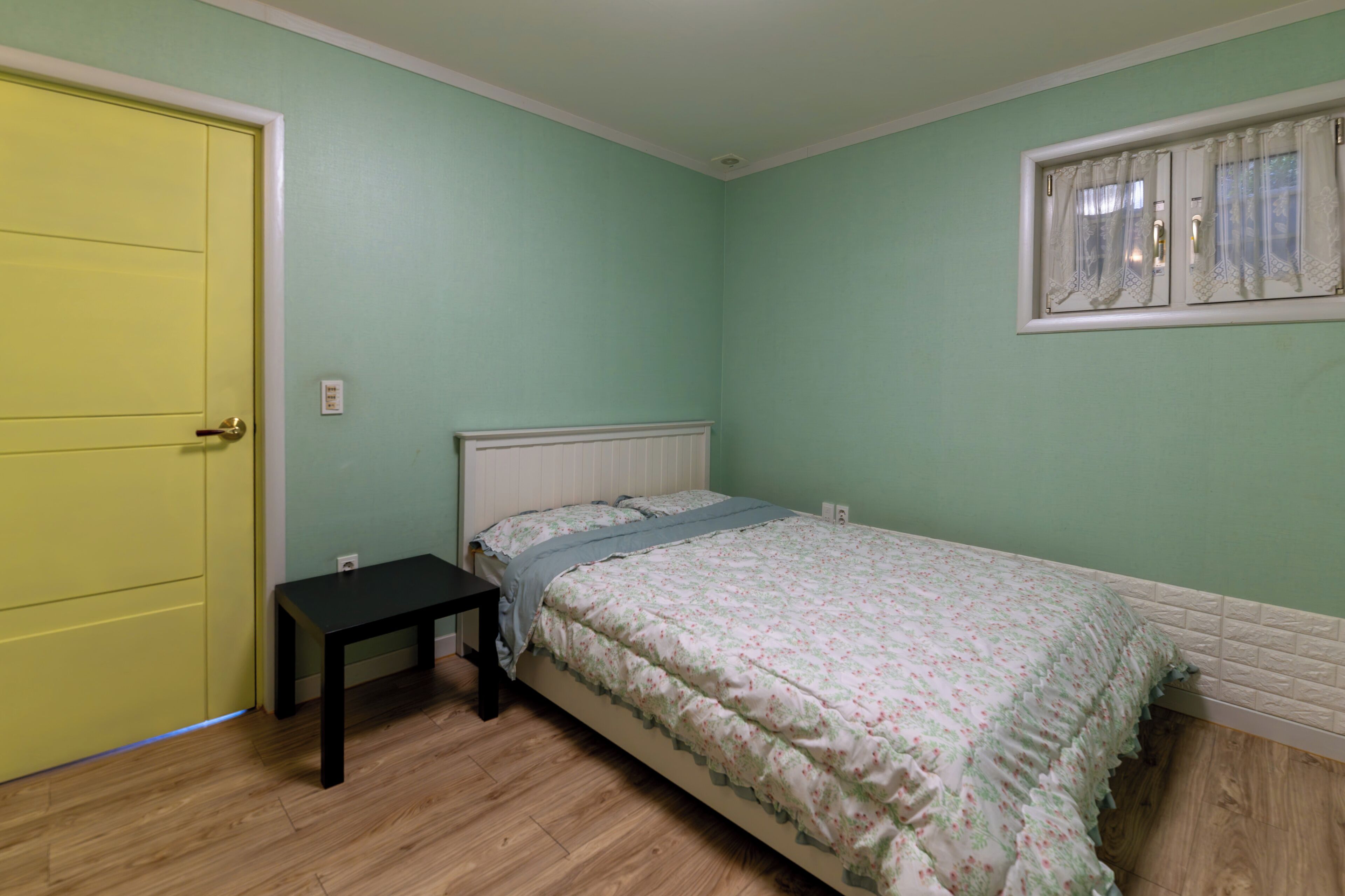 A bedroom with a bed, a bedside table, a window with curtains, and a door.