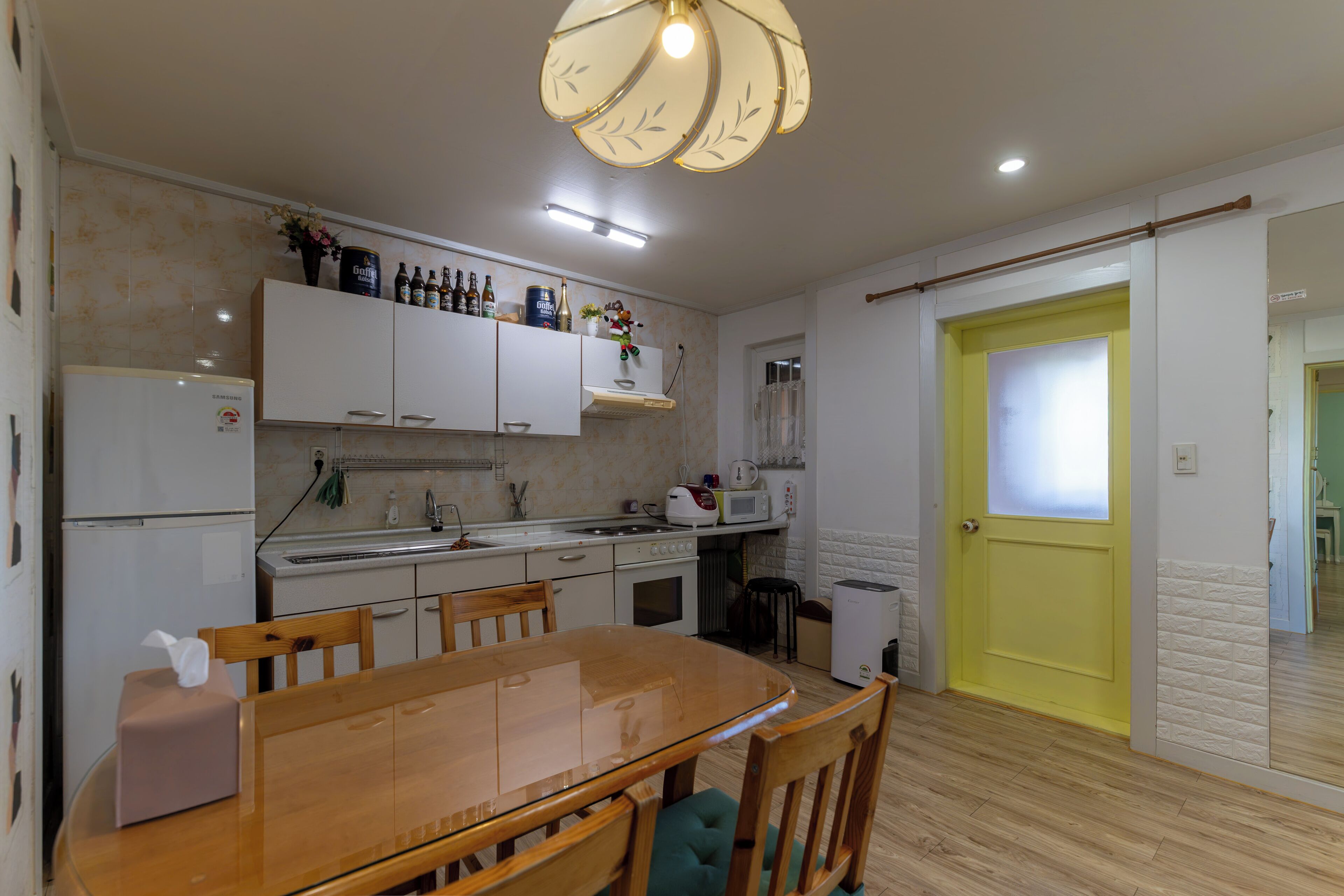 Une cuisine de taille réduite avec des meubles blancs, une table à manger en bois et une porte jaune.