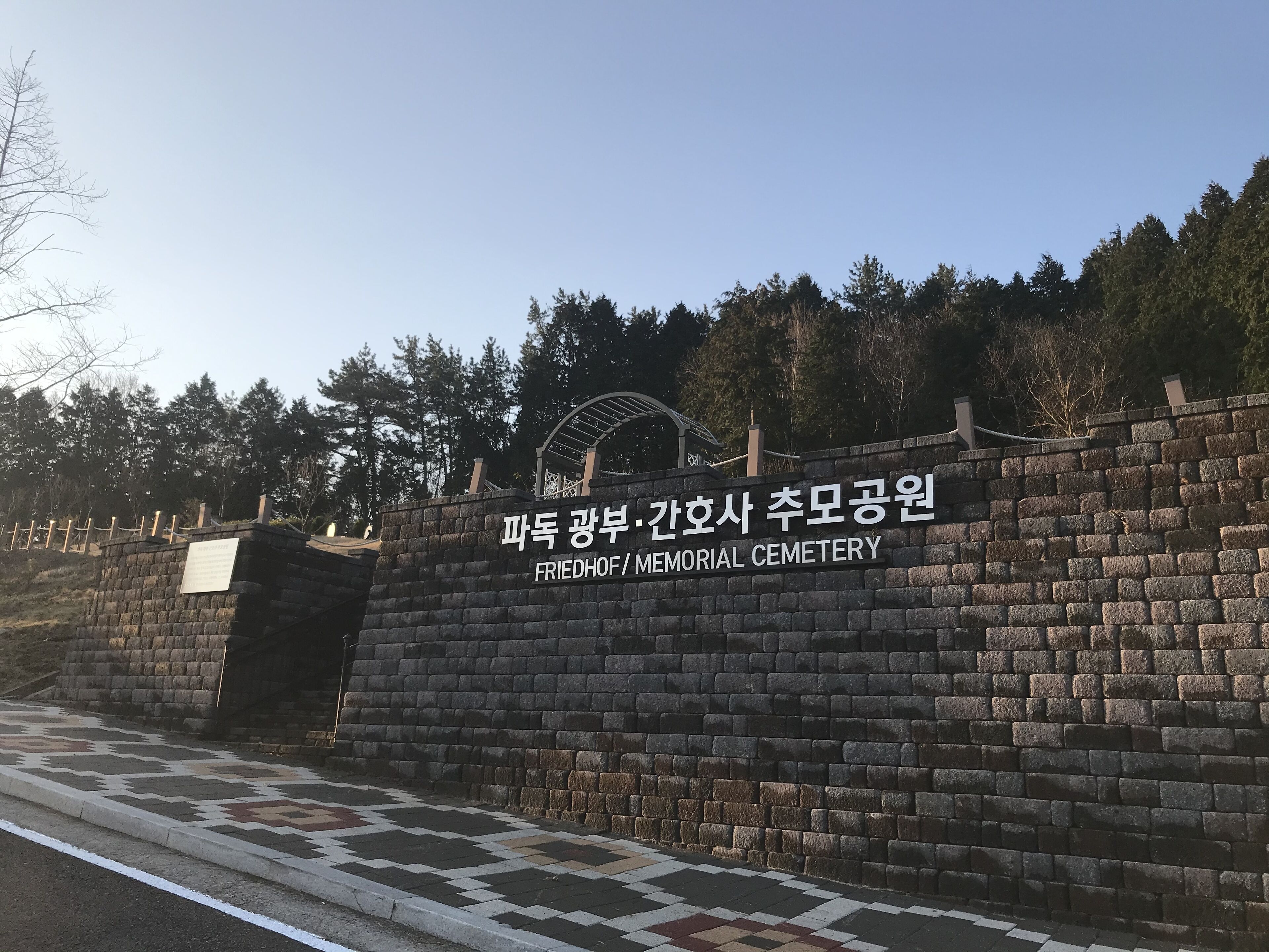 A stone wall with a sign for Friedhof / Memorial Cemetery.