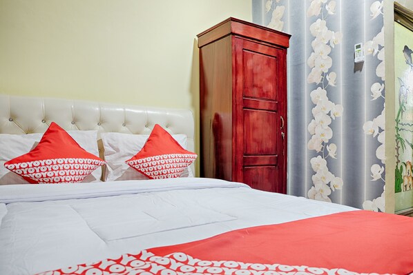 Una cama con ropa de cama blanca y roja, un armario rojo y una cortina con estampado floral.