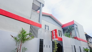 A modern building with a red and white facade, balconies, and a sign indicating it is a hotel.