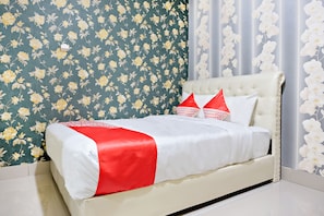 A neatly made bed with a white and red bedspread, a tufted headboard, and two pillows with red and white patterns.