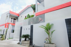 Un edificio moderno con fachada roja y blanca, entrada protegida por una reja y macetas con plantas.
