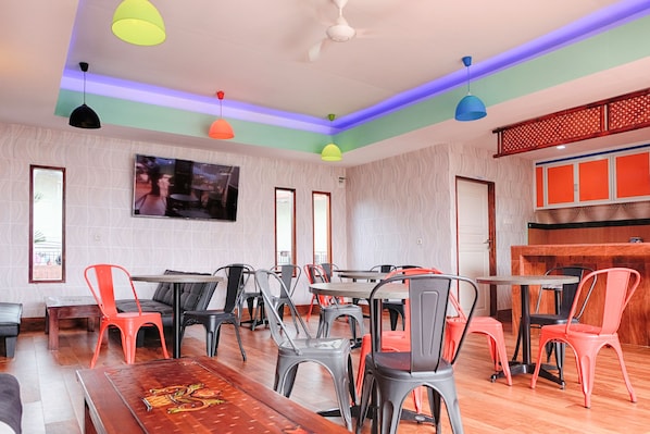 A spacious dining area with multiple tables and chairs, a ceiling fan, and a television mounted on the wall.