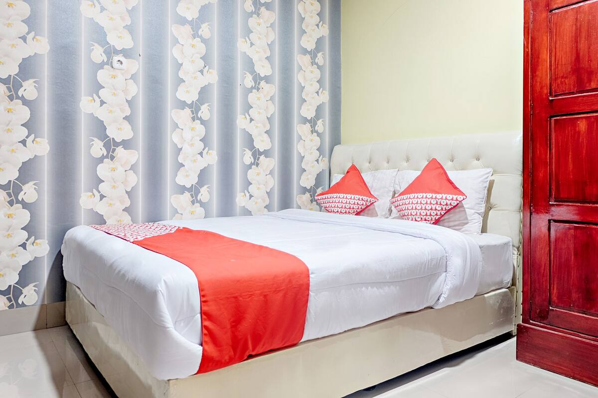 Ein Bett mit weißer und roter Bettwäsche, eine rote Tür und Vorhänge mit weißen Blumenmustern.
