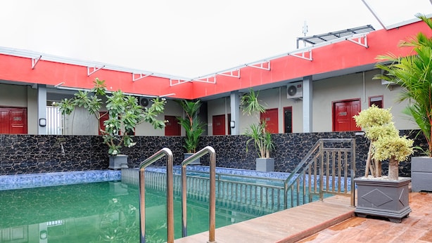 A swimming pool with a red and white building in the background, surrounded by potted plants.