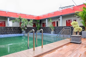 A swimming pool with a red and white building in the background, surrounded by potted plants.