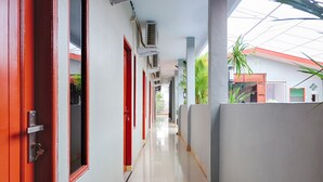 A corridor with red doors and air conditioning units, leading to a covered outdoor area with plants.