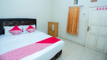 A neatly made bed with a patterned bedspread and two red pillows, a wooden cabinet, and a white door with a pink towel hanging on it.