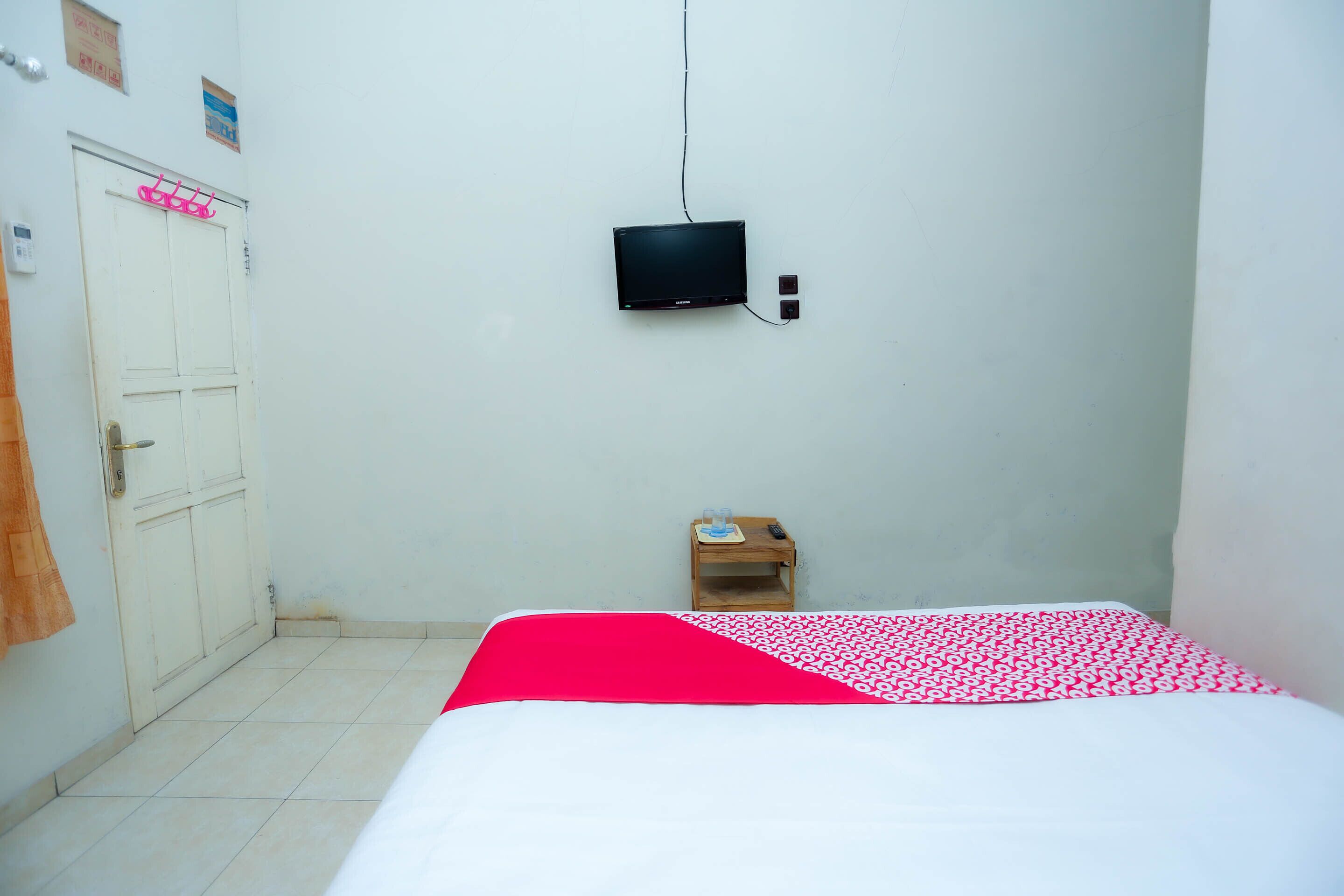 A room with a bed, a television mounted on the wall, a small wooden table, and a door.