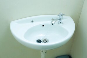 Un lavabo bianco su piedistallo con un solo rubinetto e scarico.