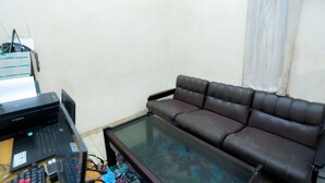 A living room with a brown leather sofa, a glass coffee table, and a desk with a printer and computer. - OYO 2692 Penginapan Mba Ros (Banjarbaru)