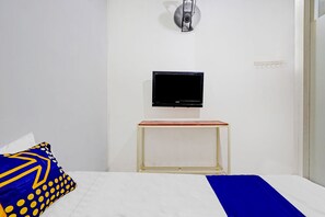A hotel room with a bed, a television mounted on the wall, and a small table with a red top. - OYO 2682 Bumi Eyang Enin Homestay Syariah (Tasikmalaya)